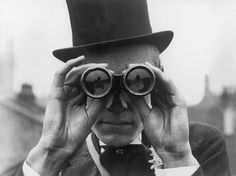 an old man wearing a top hat and holding up binoculars to look through the lens