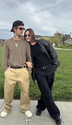 a man and woman standing next to each other on a sidewalk with grass in the background