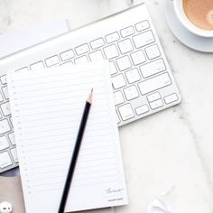 a cup of coffee next to a keyboard and mouse on a marble table with an empty notepad