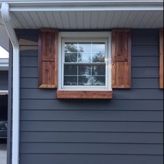 a window with wooden shutters on the side of a gray house in front of a car