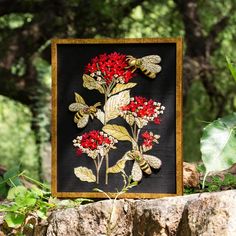 a black and gold framed painting with red flowers on it's side in the woods