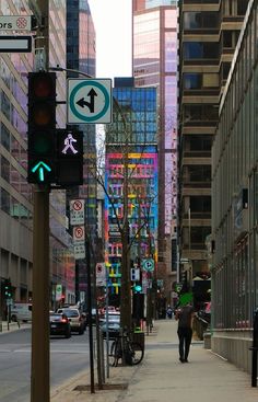 a person walking down a street next to tall buildings and traffic lights with arrows on them