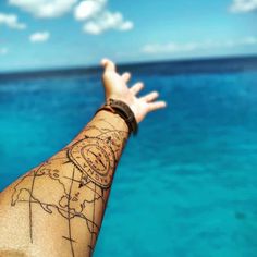 a person's arm with a map tattoo on it and the ocean in the background