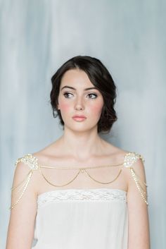 a woman wearing a white dress with pearls on her shoulders and shoulder, looking at the camera