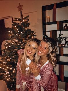 two young women standing in front of a christmas tree with their arms around each other