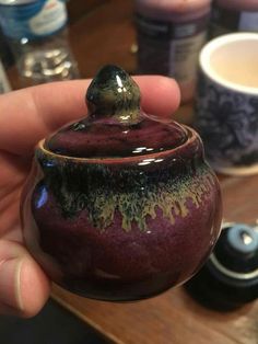 a hand holding a purple and black ceramic jar