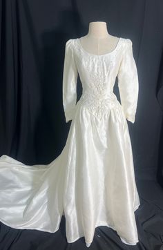 a white wedding dress with long sleeves on a mannequin head stand in front of a black backdrop