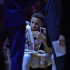 the basketball player is wiping his face with a towel on his lap while sitting in front of him