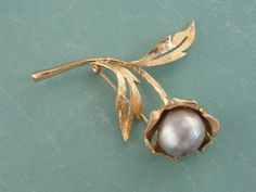 "Created in the era of the power suit, this brooch is the perfect bold statement for a lady's lapel! Brushed and etched gold forms a stylized blossom, set at the center with a large, beautiful cultured pearl of the finest quality! The color of the baroque shaped pearl is dove grey, pale and gleaming with overtones of purple and teal. Love this piece but want to make it more versatile, we here at Market Square Jewelers along with our master metalsmiths can convert this fantastic brooch into a nec Purple And Teal, Market Square, Floral Brooch, Power Suit, Dove Grey, Lily Of The Valley, Baroque Pearls, Eternity Bands, Paloma