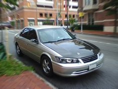 a silver car driving down a street next to tall buildings