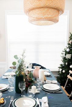 a dining room table set for christmas with plates, silverware and candles on it