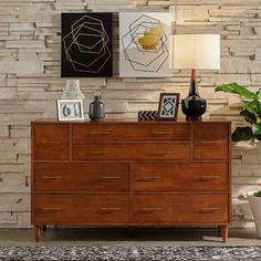 a wooden dresser sitting in front of a wall with pictures on it and a lamp next to it