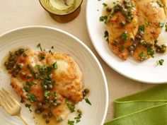 two white plates topped with chicken covered in sauce and green beans next to a glass of wine