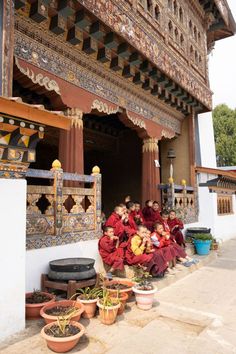 some people are sitting on the steps in front of a building with potted plants