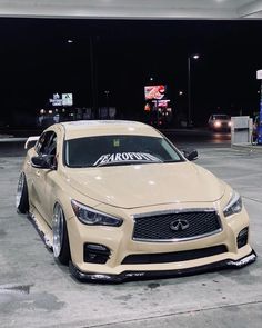 a beige car parked in front of a gas station at night with the lights on