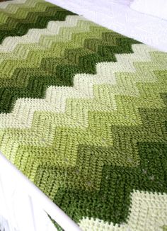 a crocheted green blanket on top of a white bed with a wooden headboard