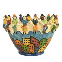 a ceramic bowl with people sitting on the edge and buildings painted on it's sides