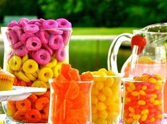 there are many candy items in the glass vases and pitcher on the table next to each other