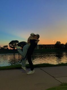 a man and woman are dancing in front of a lake at sunset or dawn with their arms around each other