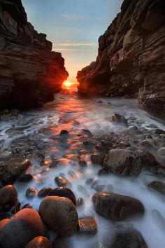 the sun is setting over some rocks in the water and there are waves coming up on them