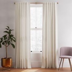 a room with a chair, potted plant and white curtain in it's corner