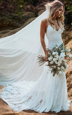 a woman in a wedding dress is holding a bouquet and posing for the camera with her veil blowing in the wind