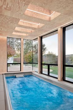 an indoor swimming pool with large windows and wood paneling on the ceiling is shown