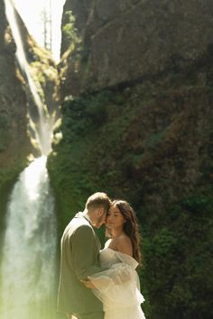 a bride and groom standing in front of a waterfall at their wedding day with sunlight streaming down on them