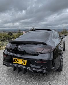 the rear end of a black sports car parked on a gravel road with dark clouds in the background