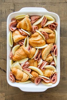 a casserole dish filled with ham, cheese and crescent roll rolls on a wooden table