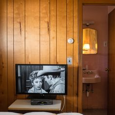 a television sitting on top of a table in front of a bathroom sink and mirror