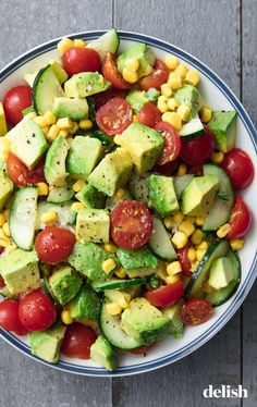 a bowl filled with cucumber, tomatoes and corn on top of a wooden table