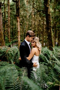 a bride and groom standing in the middle of a forest with ferns on the ground