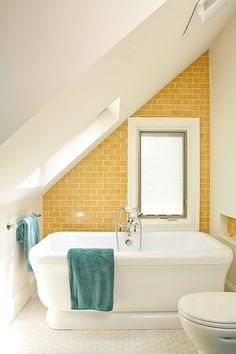 a white bath tub sitting next to a toilet in a bathroom under a slanted ceiling