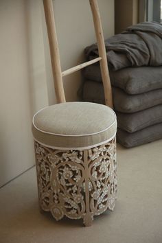 a wooden stool with a cushion on it in front of a stack of folded linens