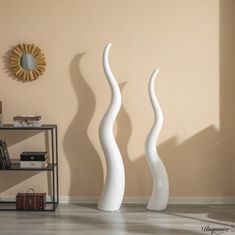 two tall white vases sitting next to each other on a hard wood floor in front of a beige wall