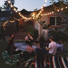 a group of people sitting on top of a blanket in front of a house at night