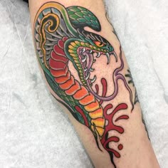 a colorful tattoo on the leg of a person with a snake in it's mouth