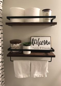 two shelves with towels, toilet paper and a welcome sign on them in a bathroom