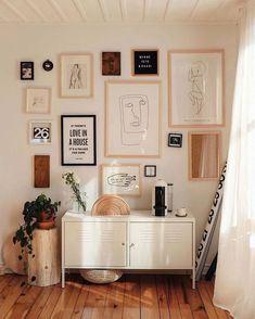 a white cabinet sitting on top of a wooden floor next to a wall covered in pictures