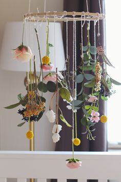 a mobile with flowers hanging from it's sides in front of a bed window