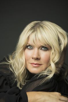 a woman with blonde hair and blue eyes is posing for a studio photo in front of a black background