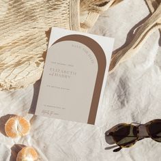 an open book and sunglasses on top of a white cloth next to some oranges