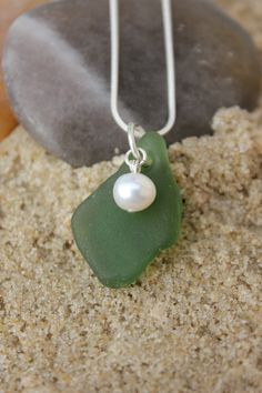 a green sea glass necklace with a pearl on it sitting on top of a rock