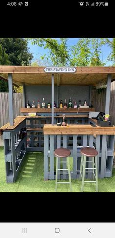 an outdoor bar made out of pallets with stools in the grass and bottles on top