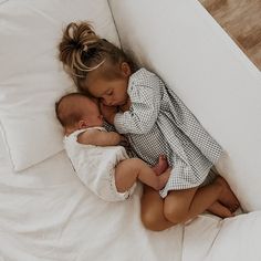 two young children laying on top of a bed next to each other, one holding the baby's head