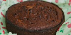 a chocolate cake sitting on top of a green and red paper wrapper with cherries around it