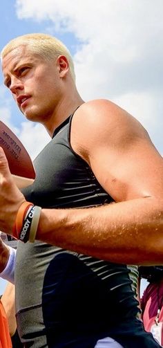 a man holding a football in his right hand and wearing an orange band around his wrist