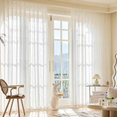 a living room filled with furniture and large windows covered in white sheer curtained curtains