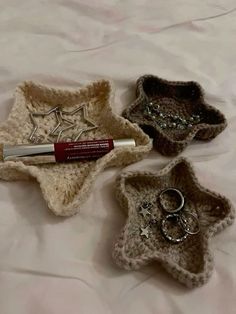 three small crocheted baskets with rings and lipstick in them on a white sheet